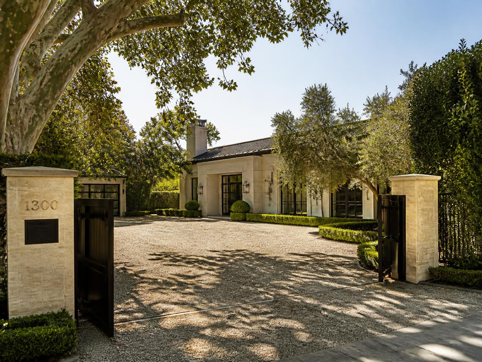 Gated Brentwood estate with limestone facade, gravel motor court and mature sycamore and olive trees